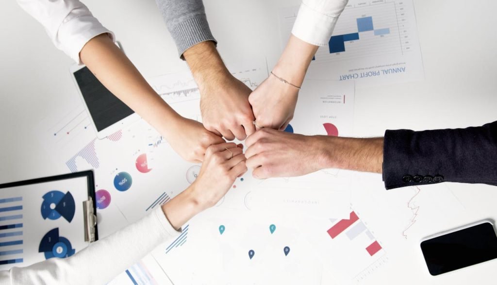 persons-hand-with-silver-ring-5716037 Colleagues celebrate success with a fist bump over financial charts depicting teamwork and unity.
